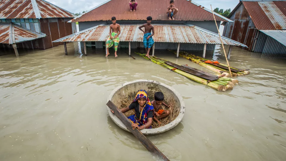 FLOODS IN BANGLADESH. A HOUSE ALMOST SUBMERGED, FAMILY MEMBERS ON THE ROOF AND IN A SMALL CORACLE