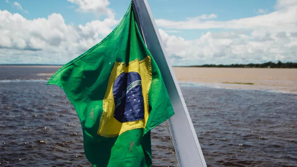 Brasilian flag held up on a boat in the Amazon. Photo: Unsplash. 