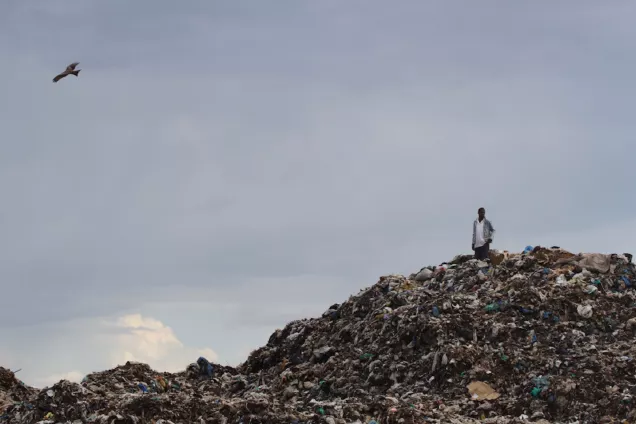 A man standing on top of a garbage dump in Kisumu, Kenya. Photo.