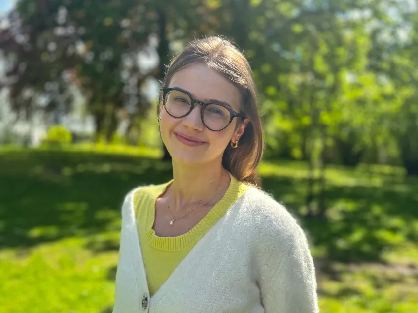 Portrait photo of a person standing outside in a park in the sun.